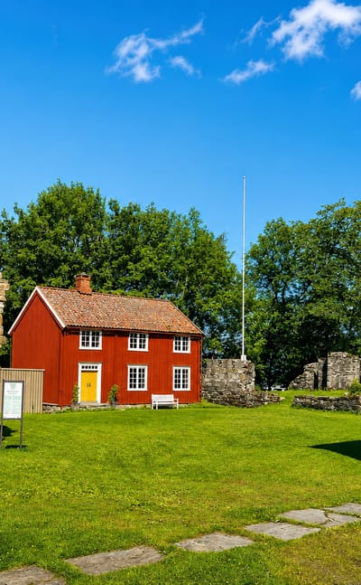Medieval stone abbey ruins beside a red timber house and lawn at Rissa in a summer courtyard