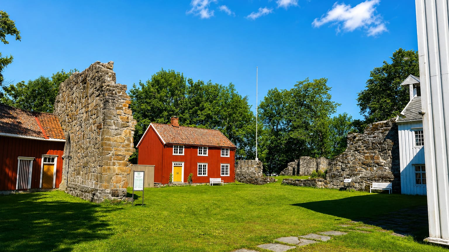 Medieval stone abbey ruins beside a red timber house and lawn at Rissa in a summer courtyard