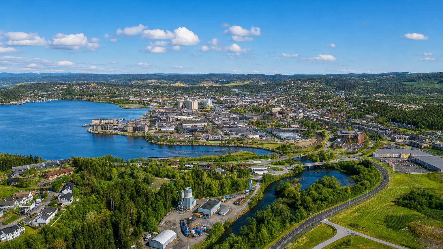Aerial view of Steinkjer, Norway, its town centre at the river mouth on the fjord, with the winding river, highway and forested hills.