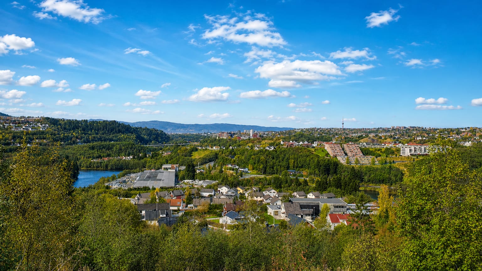 Hillside view over Fossegrenda's wooded residential area and lake toward the Trondheim skyline under a blue sky