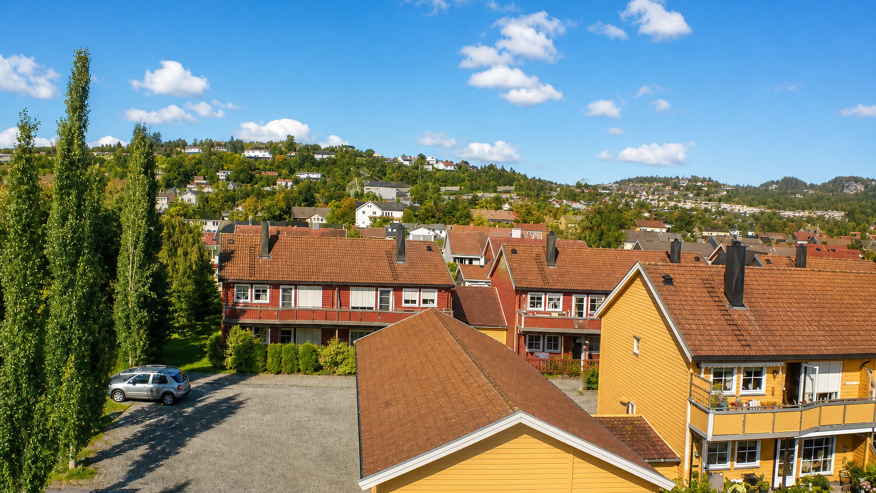 Red and yellow wooden terraced houses with tiled roofs in Nardo, Trondheim, with wooded hills behind.