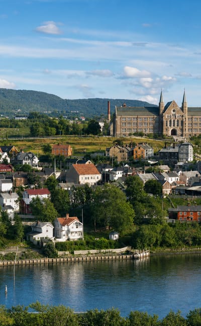 Singsaker district of Trondheim, Norway: timber houses and NTNU's castle-like main building on a green hill above the river.