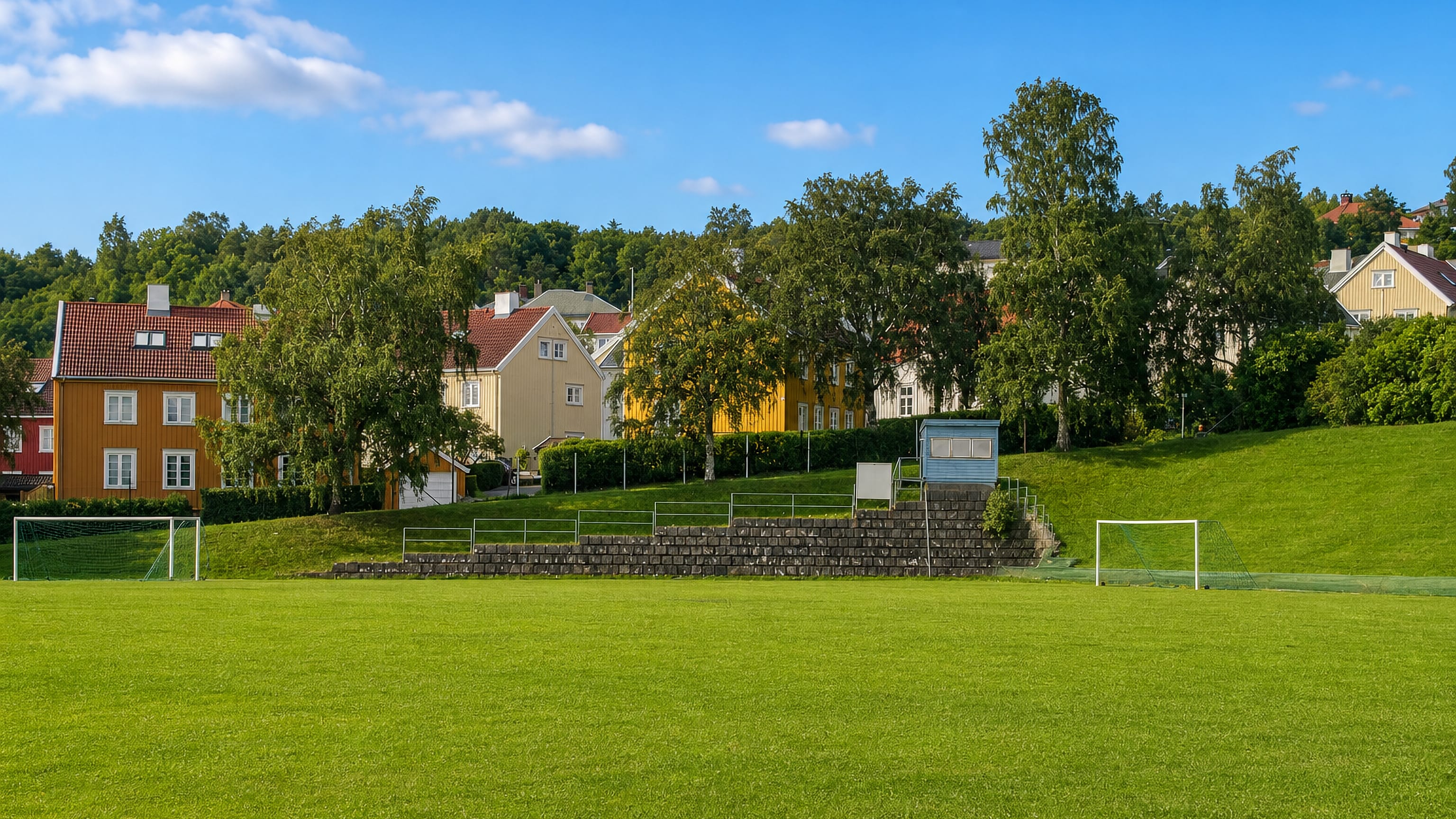 Football pitch below painted timber houses on a wooded slope in Strindheim, Trondheim.