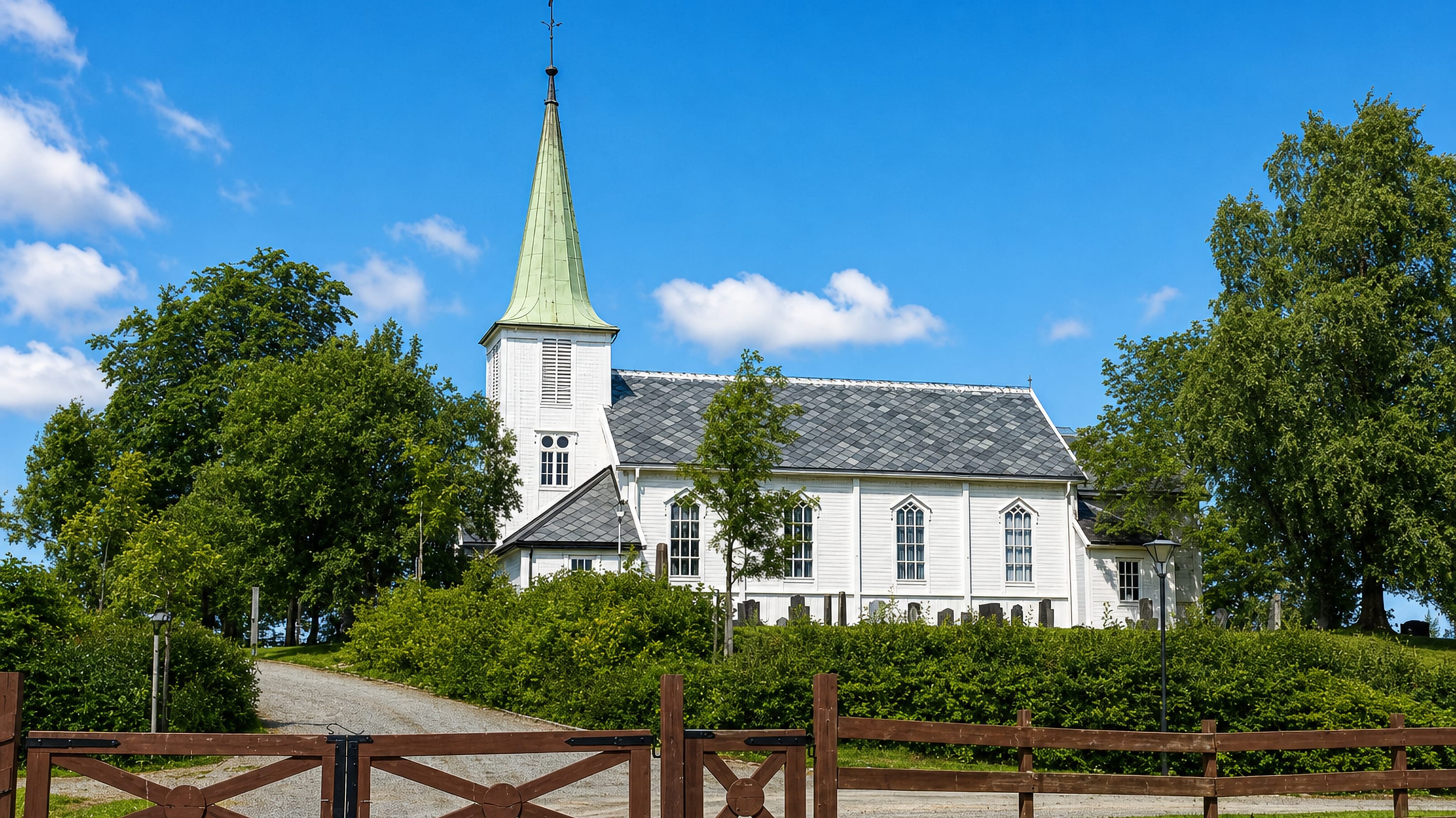 White wooden church with a green spire behind a timber gate at Tiller, on Trondheim's southern edge.