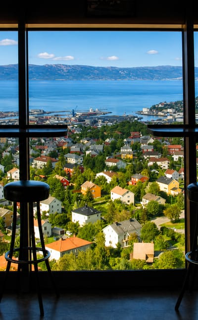 Daytime view over Trondheim and the fjord from the Tyholt Tower restaurant in Tyholt, Norway, with bar stools at the window.