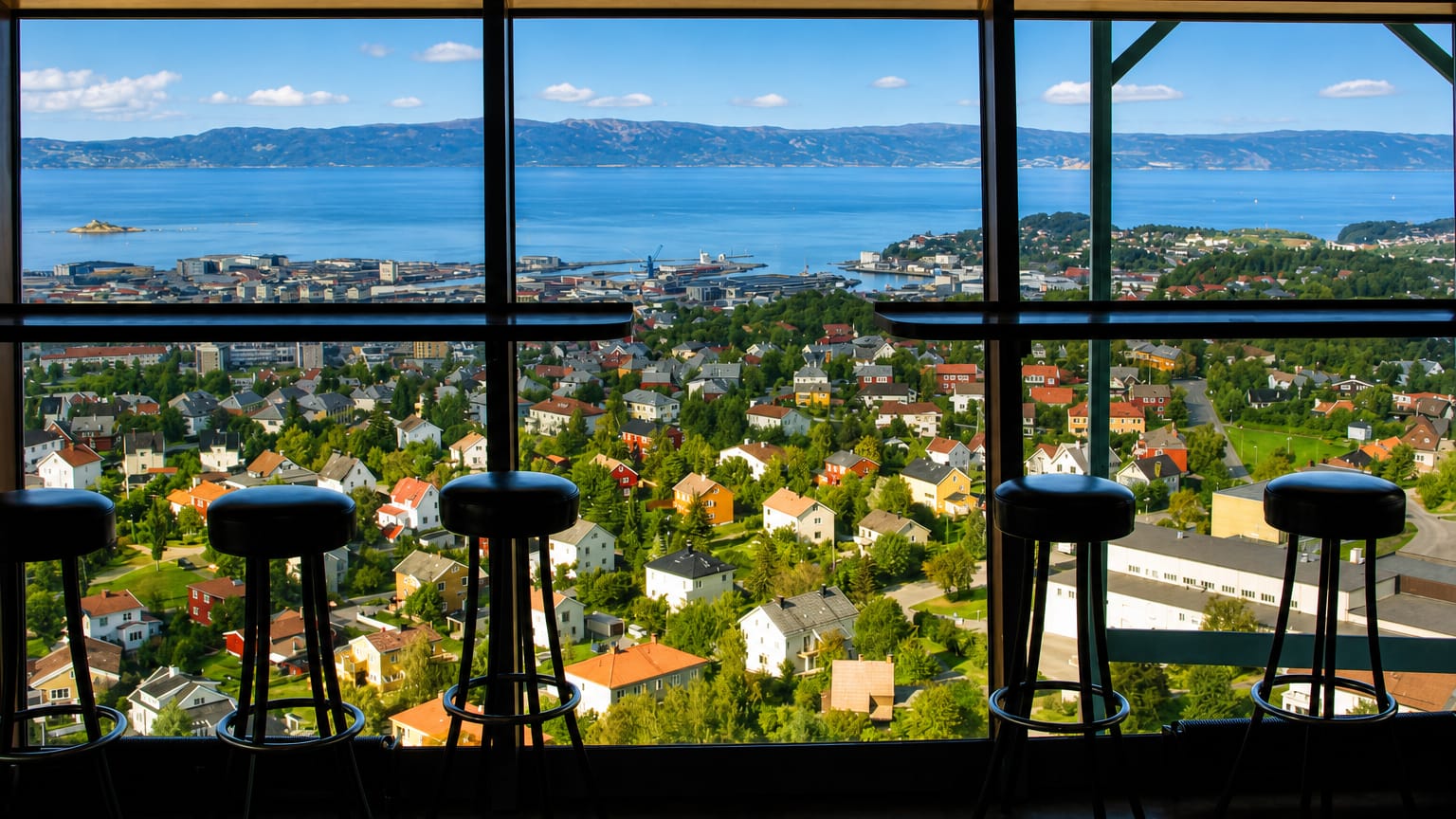 Daytime view over Trondheim and the fjord from the Tyholt Tower restaurant in Tyholt, Norway, with bar stools at the window.