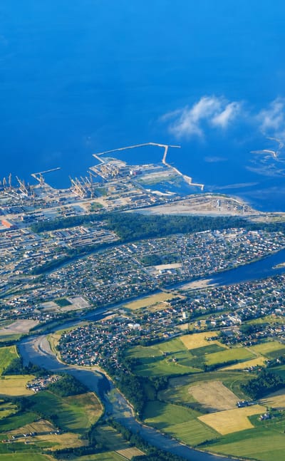Aerial view of Verdal, Norway, with a river delta, green farmland, and an industrial harbour on the fjord.
