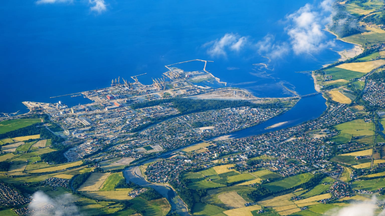 Aerial view of Verdal, Norway, with a river delta, green farmland, and an industrial harbour on the fjord.