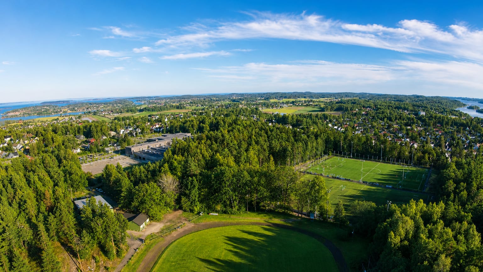 Aerial view over Borgheim, Norway, showing forests, football pitches and scattered houses near the Vestfold coastline.