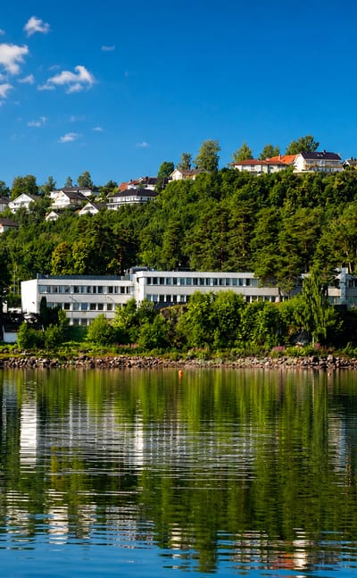 Calm fjord waterfront at Horten, Norway, with white and red houses on a wooded hillside mirrored in the water.