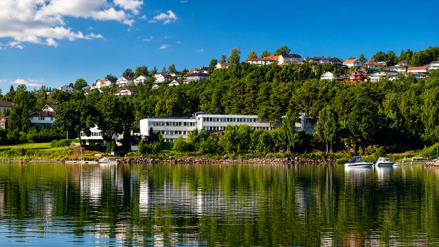 Calm fjord waterfront at Horten, Norway, with white and red houses on a wooded hillside mirrored in the water.