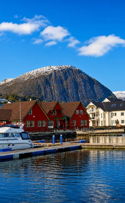 Askvoll, Norway: harbour with moored boats, colourful wooden houses and a white church below a snow-capped mountain.