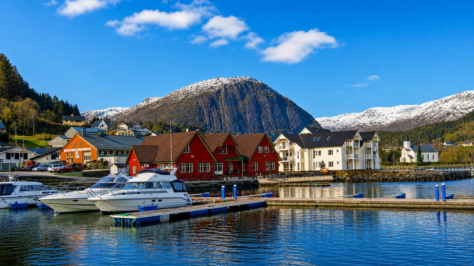 Askvoll, Norway: harbour with moored boats, colourful wooden houses and a white church below a snow-capped mountain.
