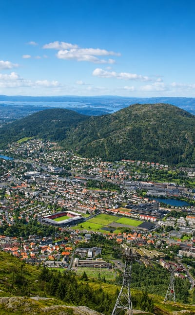 Elevated view over Landås, Norway, a residential valley district of Bergen ringed by forested hills with a sports stadium and distant lakes