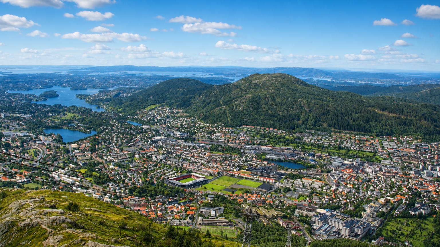 Elevated view over Landås, Norway, a residential valley district of Bergen ringed by forested hills with a sports stadium and distant lakes