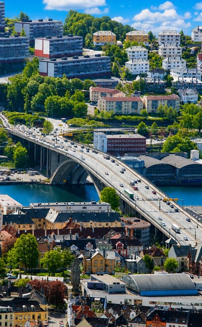 Aerial daytime view of Møhlenpris, Bergen, with an arched bridge crossing the Puddefjord amid dense hillside housing.