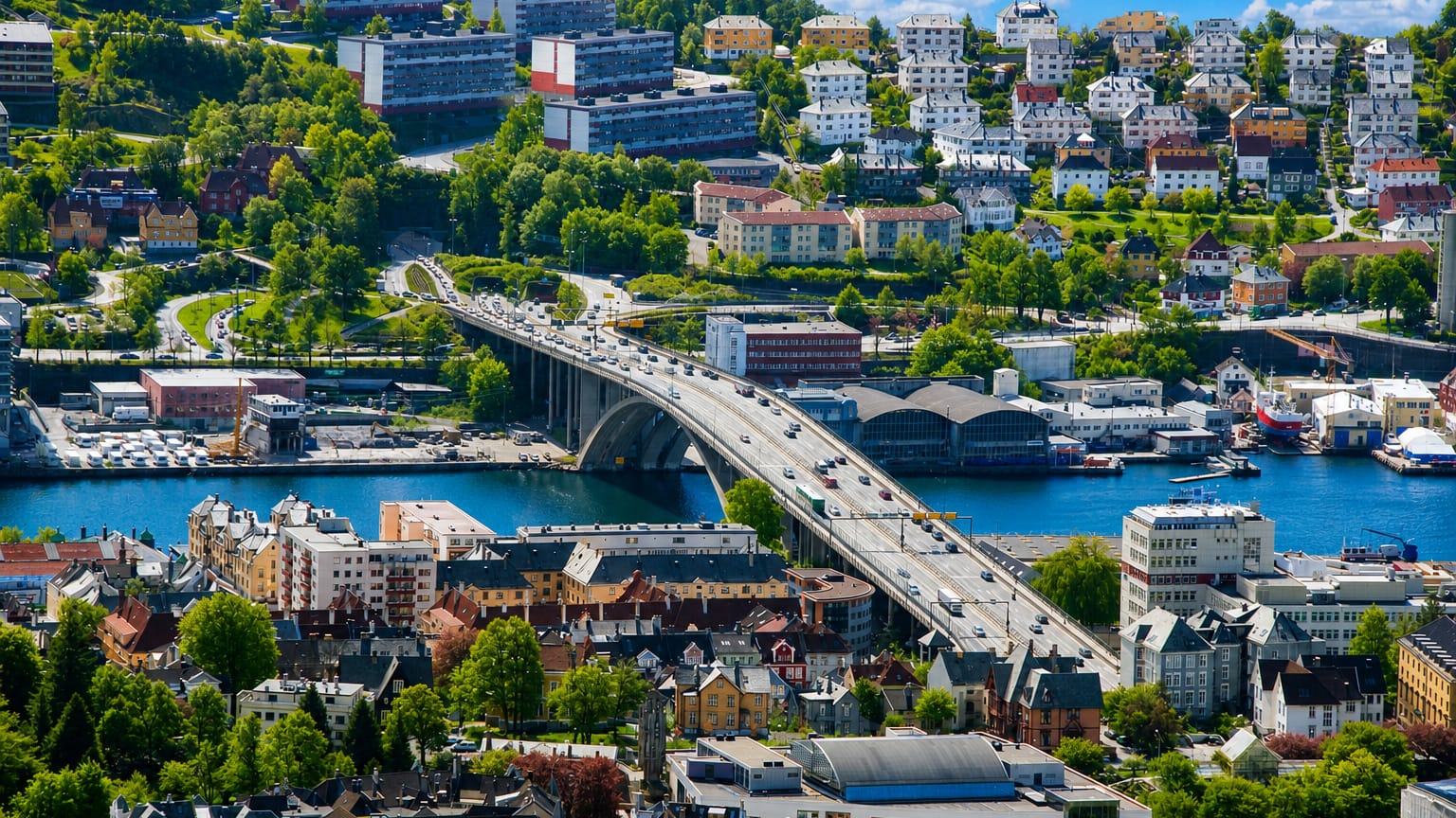 Aerial daytime view of Møhlenpris, Bergen, with an arched bridge crossing the Puddefjord amid dense hillside housing.