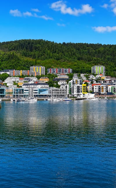 Waterfront townscape of Solheim, Bergen, with colorful modern buildings and a marina below the forested Løvstakken hill.