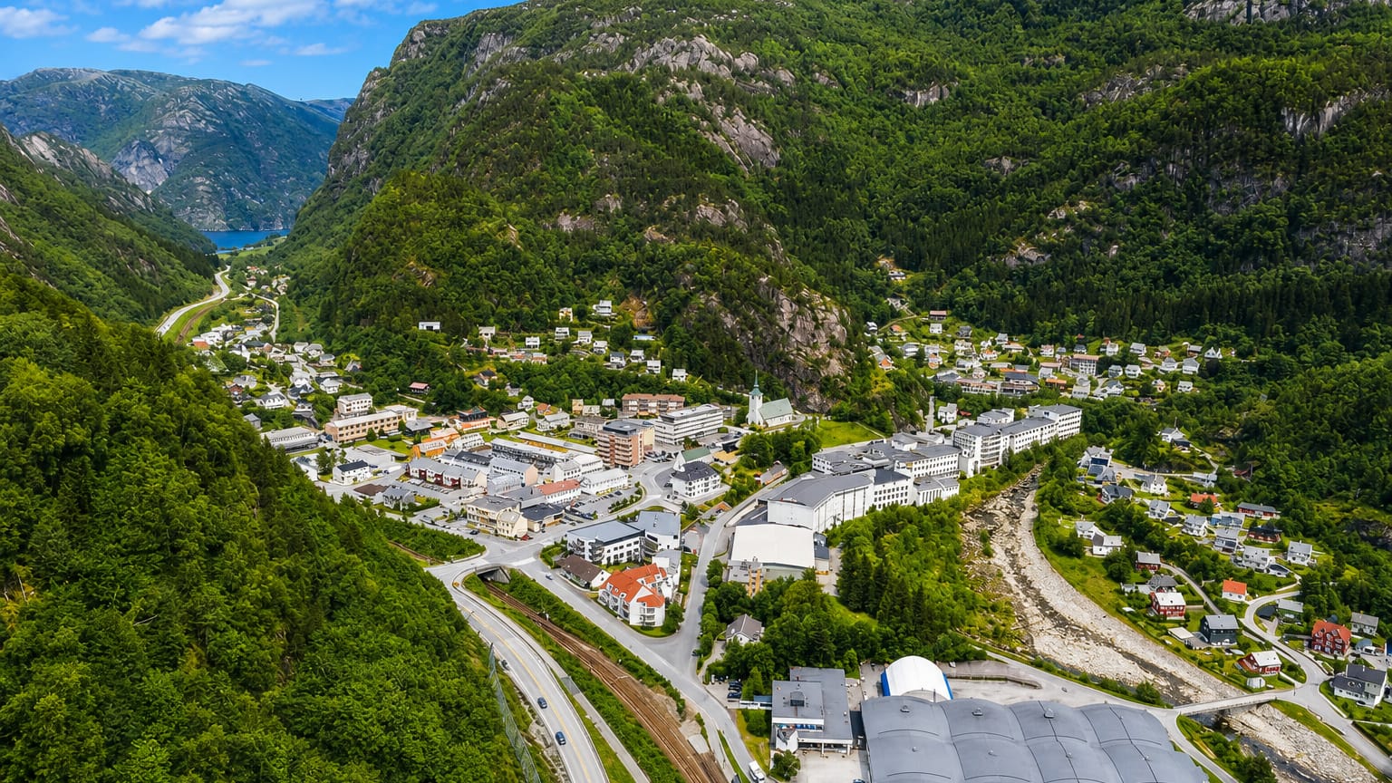 Aerial view of Dale in Vaksdal, Norway, a valley village with industrial buildings and homes below steep forested mountains.