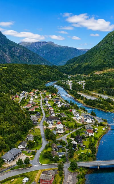 Aerial view of Eidfjord, Norway, nestled in a green valley where the river meets the fjord below steep forested mountains.