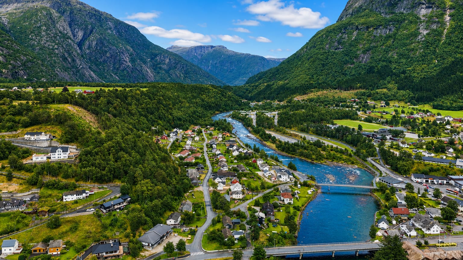Aerial view of Eidfjord, Norway, nestled in a green valley where the river meets the fjord below steep forested mountains.