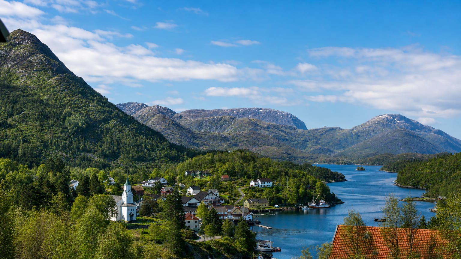 Eivindvik's white wooden church above a calm fjord, ringed by forested mountains and scattered houses under a blue sky.