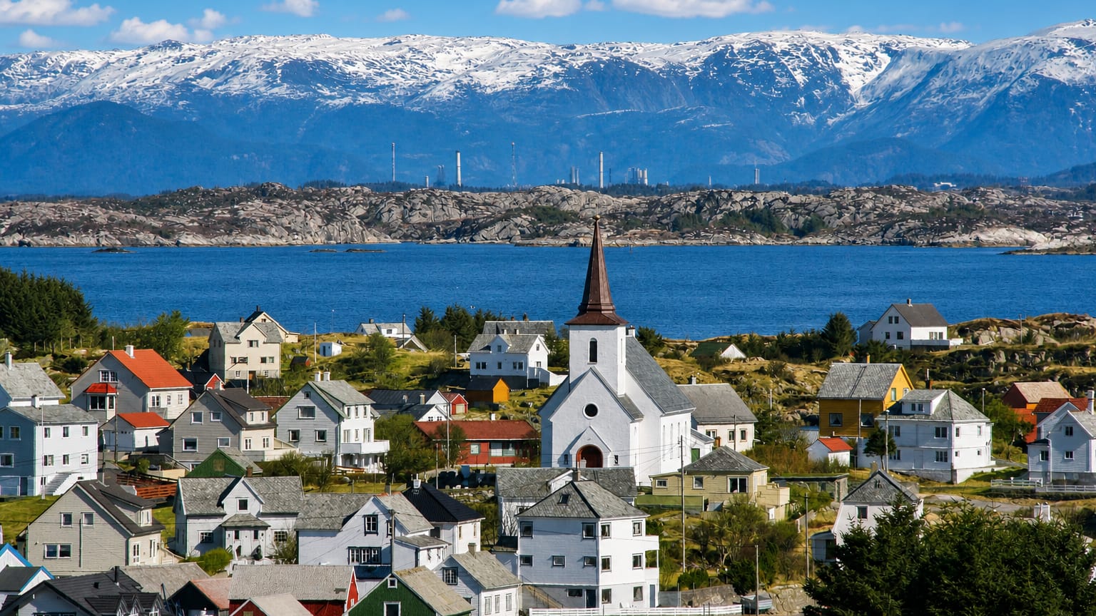 Colorful wooden houses and a white steepled church by the sea in Fedje, Norway, with distant snow-capped mountains.