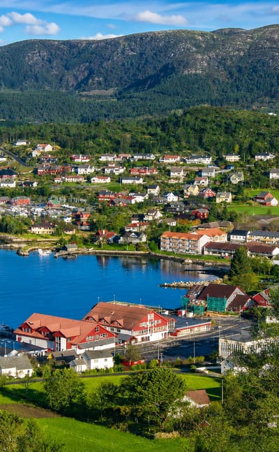 Fitjar village on its coastal sound, with a small harbor, white wooden houses and forested mountains behind
