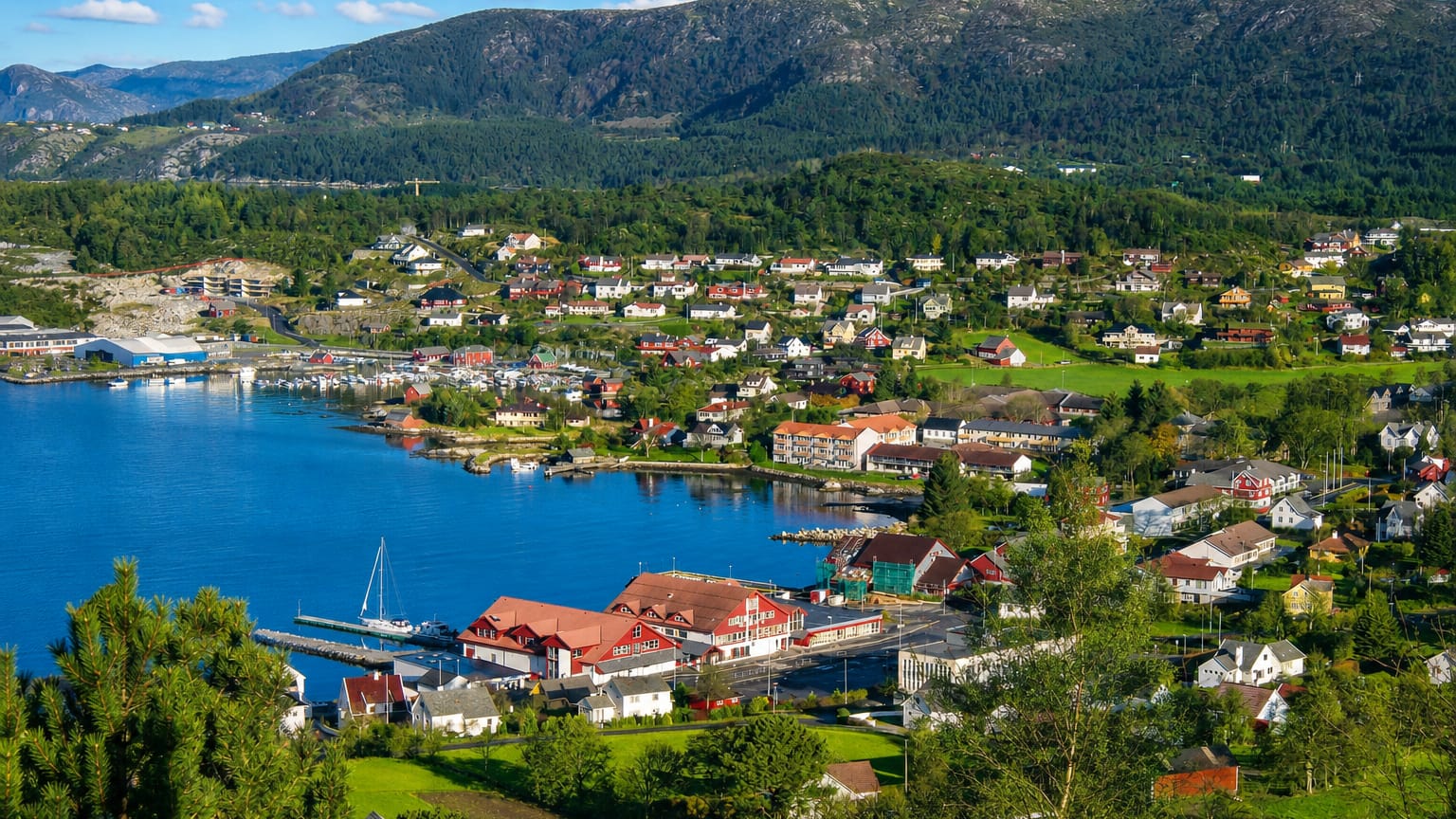 Fitjar village on its coastal sound, with a small harbor, white wooden houses and forested mountains behind