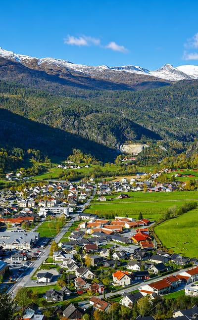Elevated view of Gaupne, Norway, a valley village ringed by snow-capped mountains and green farmland.