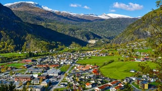 Elevated view of Gaupne, Norway, a valley village ringed by snow-capped mountains and green farmland.