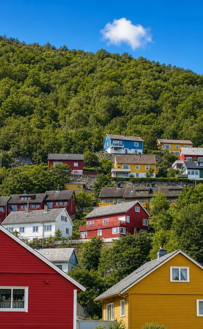 Colorful red, yellow and white wooden houses climbing a steep forested hillside in Høyanger, Norway.