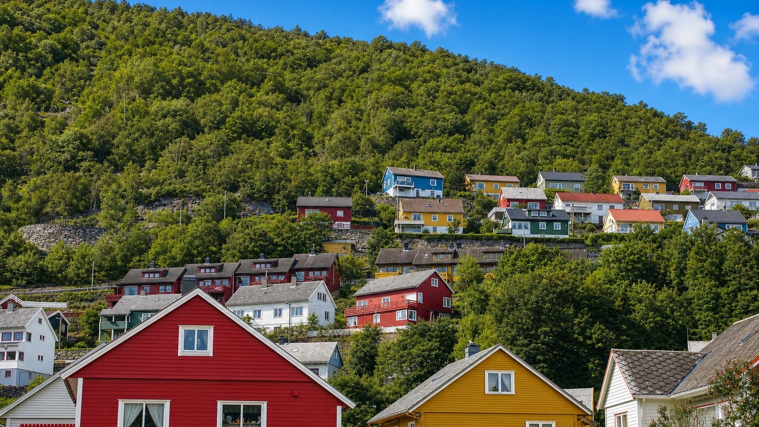 Colorful red, yellow and white wooden houses climbing a steep forested hillside in Høyanger, Norway.