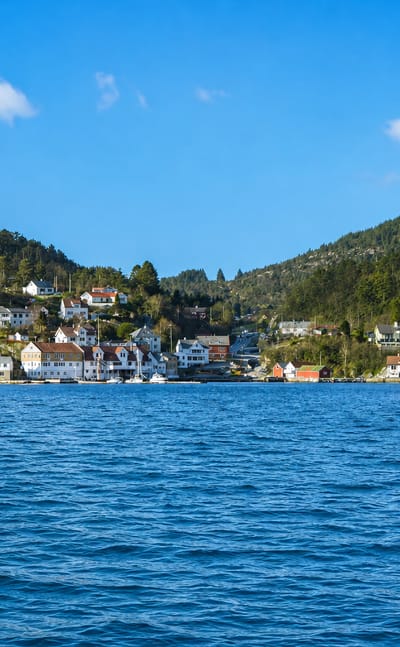 Isdalstø's white waterfront houses below forested hills along a blue fjord in Vestland, Norway