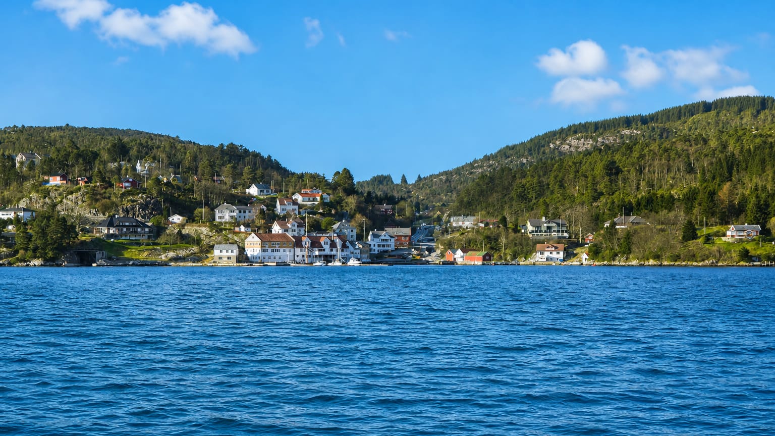 Isdalstø's white waterfront houses below forested hills along a blue fjord in Vestland, Norway