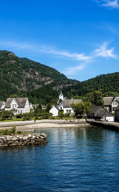Jondal village on the Hardangerfjord, white wooden houses and a steepled church below forested mountains
