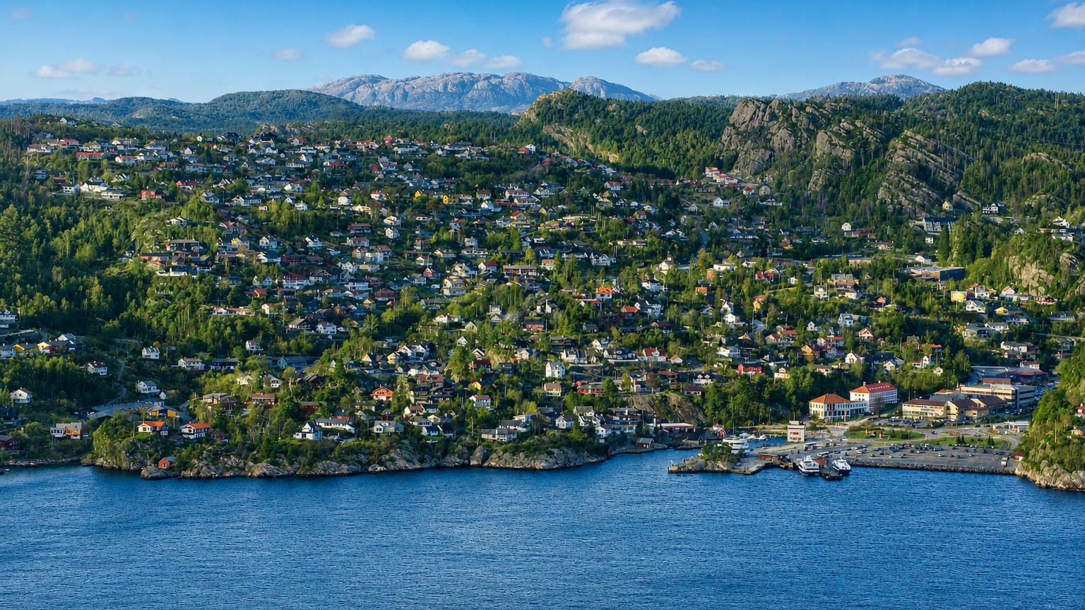Kleppestø's hillside of wooden houses above the fjord, with the ferry terminal at right and forested mountains beyond