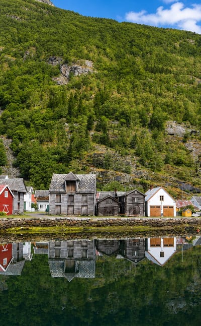 Old red, white and weathered-timber wooden houses lining the calm fjord at Lærdalsøyri, Norway, below steep forested mountains