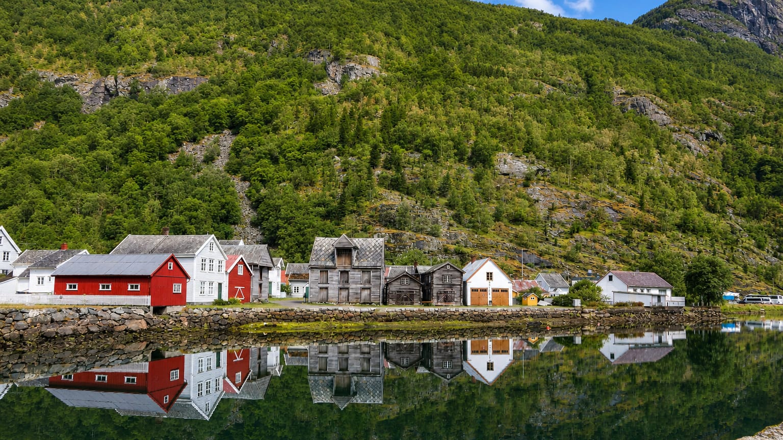 Old red, white and weathered-timber wooden houses lining the calm fjord at Lærdalsøyri, Norway, below steep forested mountains