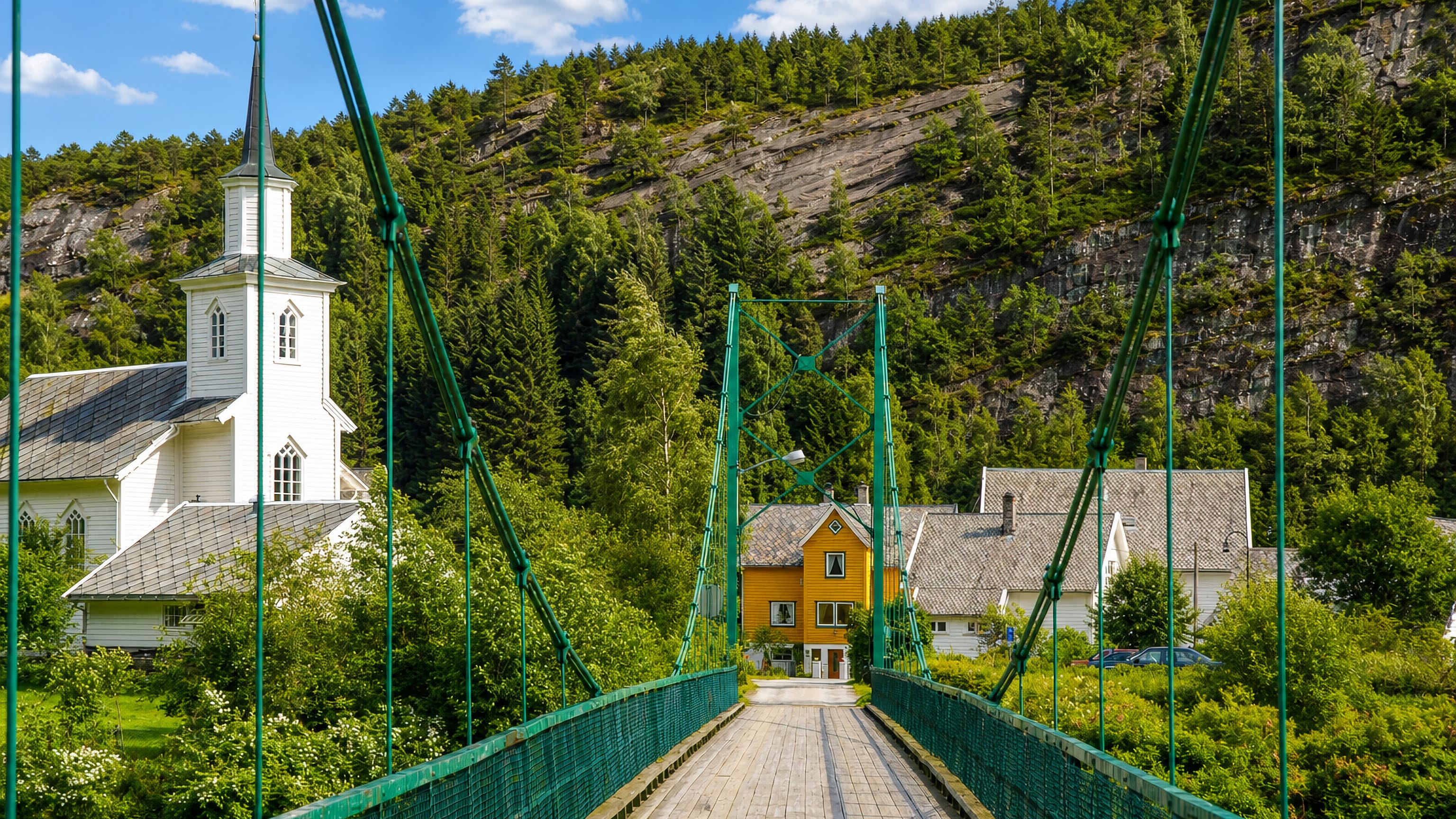 Green suspension footbridge to Mo's white wooden church and yellow houses below a forested hillside, Norway
