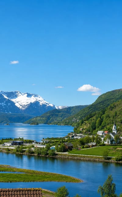 Naustdal, Norway, a fjord village with a white church beside blue water below snow-capped Vestland mountains.