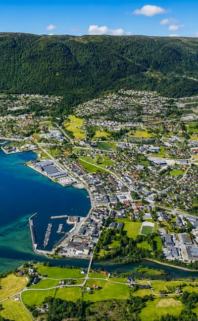 Aerial view of Nordfjordeid, Norway, its harbour and river delta beside a fjord below forested mountains
