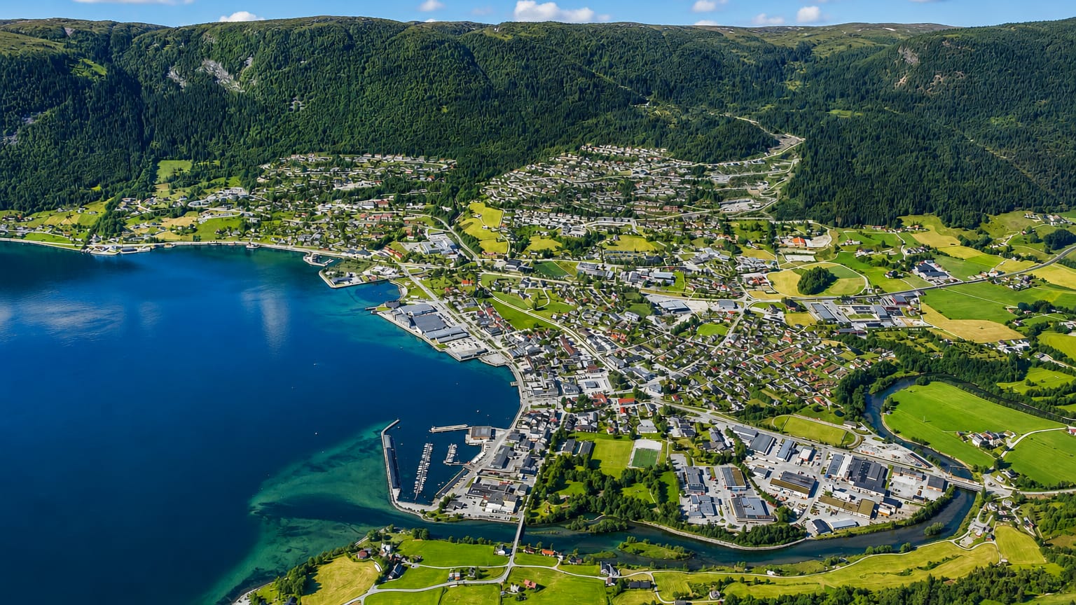 Aerial view of Nordfjordeid, Norway, its harbour and river delta beside a fjord below forested mountains