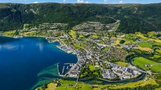 Aerial view of Nordfjordeid, Norway, its harbour and river delta beside a fjord below forested mountains