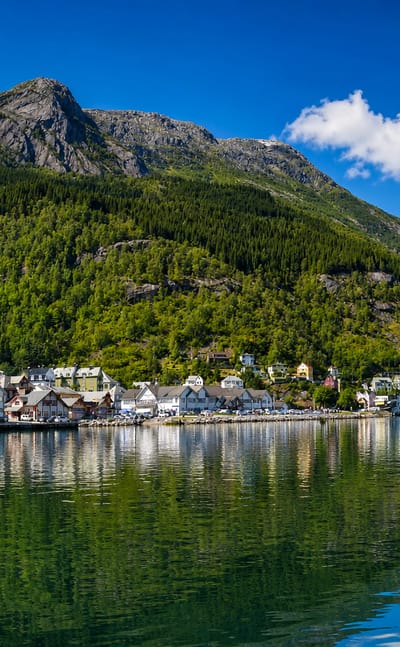 Colourful waterfront houses of Odda reflected in the Sorfjord below a steep green Hardanger mountainside