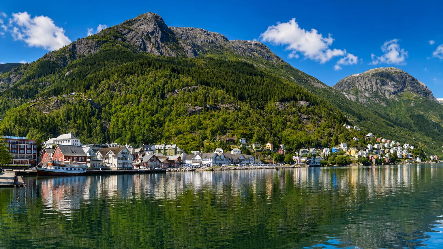 Colourful waterfront houses of Odda reflected in the Sorfjord below a steep green Hardanger mountainside