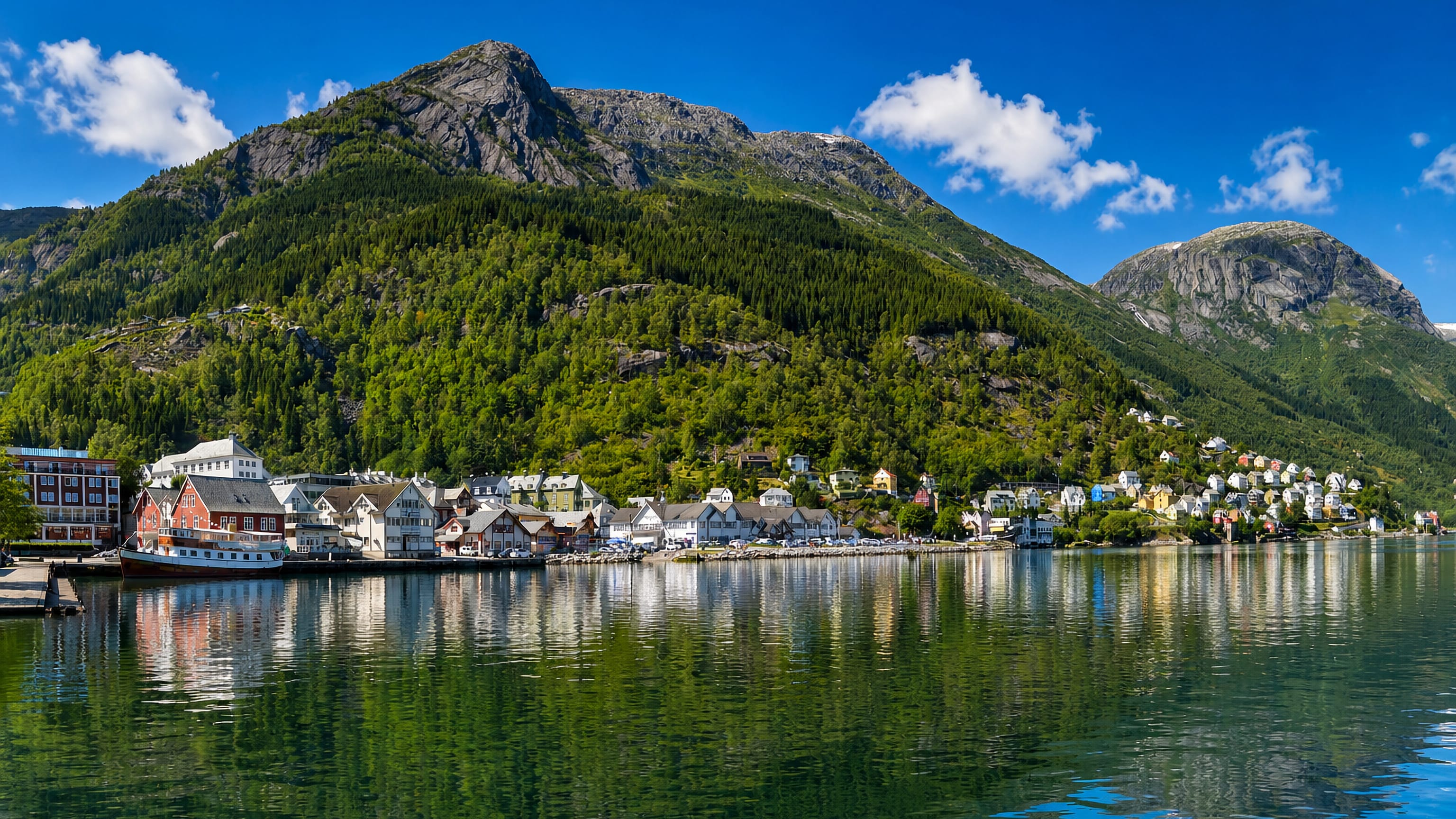 Colourful waterfront houses of Odda reflected in the Sorfjord below a steep green Hardanger mountainside