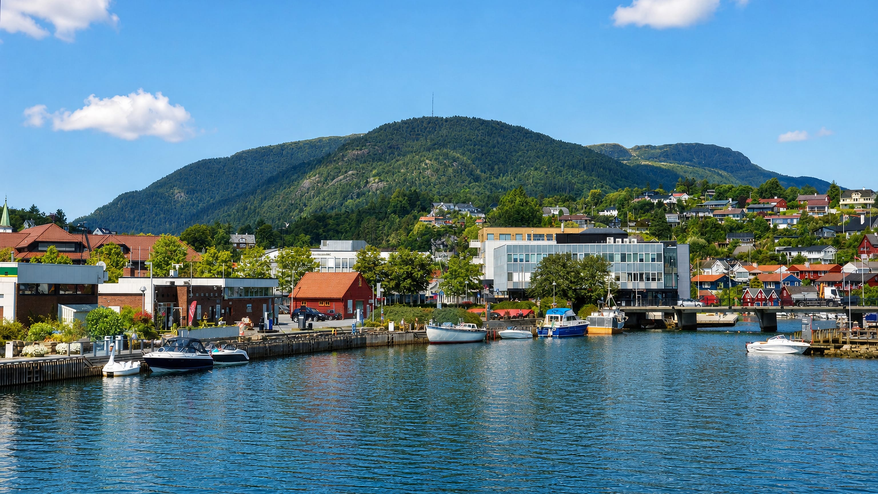 Boats moored along the harbour of Osoyro below a forested mountain, Norway