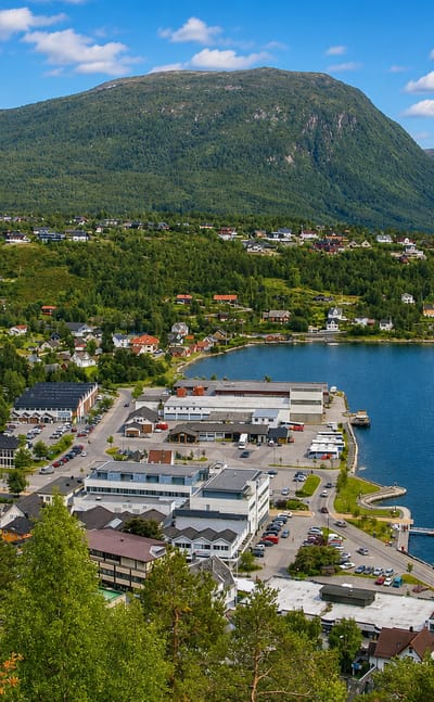 Aerial view of Sandane's waterfront town and harbor beneath forested mountains on a fjord in Vestland, Norway