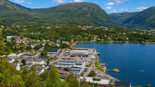 Aerial view of Sandane's waterfront town and harbor beneath forested mountains on a fjord in Vestland, Norway